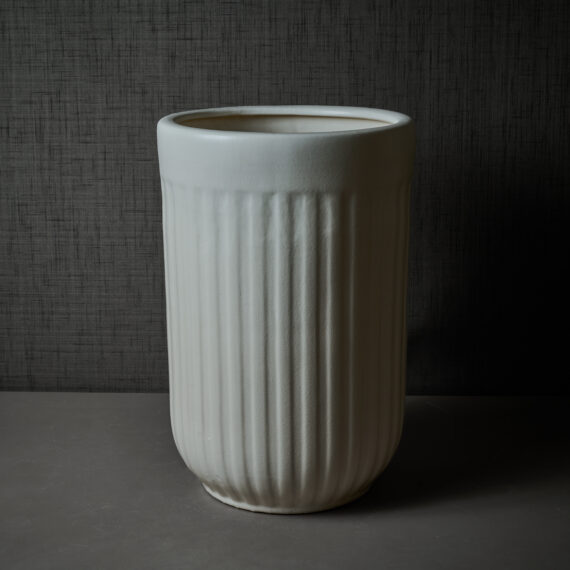 A tall, off-white ceramic planter featuring a ribbed texture on the upper section and vertical grooves on the lower section